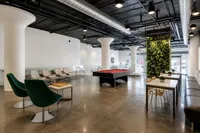 Modern communal space boasting sleek seating, a vibrant green wall, and a stylish billiards table under industrial-chic ceilings.