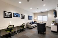 Modern lounge area with stylish decor, featuring a cozy sofa, artistic wall frames, and a functional workspace with green chairs.