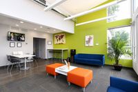 Modern lobby with vibrant green accent wall, stylish blue and orange seating, and natural light from large windows.