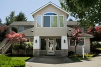 Charming two-story home with elegant stone accents, surrounded by vibrant landscaping and mature trees.