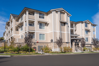 Modern three-story apartment building with balconies and lush landscaping under a clear blue sky.