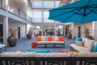 Inviting outdoor lounge space with stylish seating, vibrant cushions, large planters, and expansive blue umbrella for shaded relaxation.