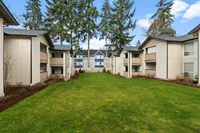 Open landscaped courtyard at Boardwalk at University Place surrounded by renovated apartment homes and tall evergreen trees.