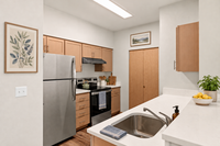 Staged kitchen with stainless steel appliances, light wood cabinets, white countertops, framed artwork, and greenery.