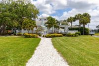 Tradition at Palm Aire Luxury Apartments for Rent in Sarasota FL - Tradition at Palm Aire - Building Exterior with White Walls, Fence, Grassy Lawn, Palm Trees, and Gravel Path