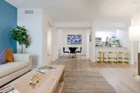 Tradition at Palm Aire Apartments for Rent in Sarasota, FL - Tradition at Palm Aire - Furnished Living Area with Vinyl Plank Flooring, Area Rug, Sofa, Wooden Cofee Table, Blue Accent Wall, House Plant, and View of Dining Area and Kitchen
