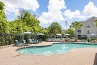 Port Royal, SC, Apartments Near Air Station - Preserve at Port Royal - Resort Style Swimming Pool With Paver Sundeck, Lounge Chairs, Shade Umbrellas, Palm Trees, And Community Buildings.