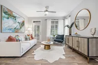 Port Royal, SC, Apartments Near Sands Beach - Preserve at Port Royal - Bright Living Room With White Sofa, Ceiling Fan, Large Windows With Sheer Curtains, And Media Console With Round Mirror.