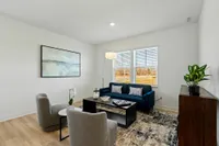 Townhomes with Attached Garage in Brownsburg, IN - Wynne Farms - Living Room With A Blue Sofa, Large Windows, Wood Style Flooring, And A Potted Plant.