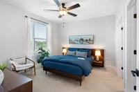 North Chesterfield, VA, Pet-Friendly Apartments - The James at Springline - A Bedroom with Nightstands, Lamps, Ceiling Fan, Large Window, Dresser, and Indoor Plant.