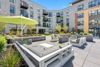 High-End Apartments in Richmond, VA - The James at Springline - An Outdoor Courtyard with Cushioned Lounge Seating, Patio Tables, Umbrellas, String Lighting, and Landscaped Planters.