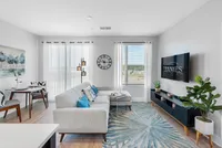 North Chesterfield, VA, Apartments Near Chesterfield Town Center - The James at Springline - A Living Room with a Sectional Sofa, Wall-Mounted TV, Large Windows, and Indoor Plants.