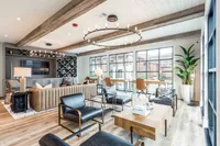 A modern lounge area featuring comfortable seating, wooden beams, and large windows that allow natural light to fill the space. A decorative plant and stylish light fixtures add to the inviting atmosphere.