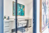 A modern office featuring a sleek desk, a white chair, and colorful abstract artwork on the walls. Natural light fills the space, creating a bright and inviting atmosphere.