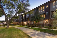 Exterior homes surrounded by trees and a landscaped pathway, is shown during twilight. The warm lights from the windows create a welcoming atmosphere.