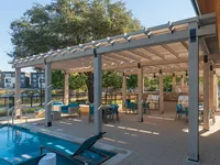 A shaded outdoor seating area with tables and chairs next to a swimming pool, surrounded by trees and a scenic view. The space is designed for relaxation and social gatherings.