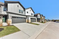 Dog-Friendly Townhomes in North Austin, TX - Lone Oak Homes - Street View Of Modern Townhome Buildings With Attached Two Car Garages, Private Driveways, Sidewalks, And Clear Blue Sky.
