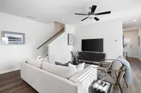Pet-Friendly Townhomes in Cartersville, GA - Brightside at Cloverleaf - Living Room With Wood-Inspired Luxury Plank Flooring, A Sectional Sofa, Television Console, Armchairs, And A Ceiling Fan.