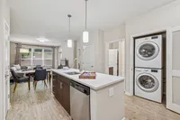 Kitchen island with brown cabinetry and stackable washer and dryer