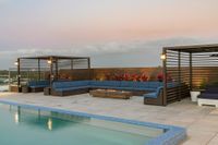 Elegant rooftop patio with modern cabanas, a cozy fire pit, and a refreshing pool set against a serene sunset sky.