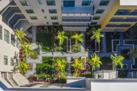 Stunning aerial view of a contemporary apartment complex courtyard, featuring lush green lawns, vibrant flower beds, and elegant palm trees.
