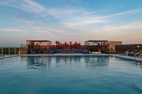 Luxurious rooftop pool with modern cabanas, surrounded by lush plants, under a serene evening sky.