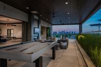 Luxurious rooftop patio with elegant lounge area, pool table, and stunning city skyline views at sunset.