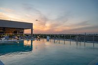 Luxurious rooftop pool with elegant lounge chairs overlooking a stunning sunset view.