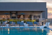 Chic rooftop pool area with modern lounge chairs and umbrella seating, offering a serene sunset view.