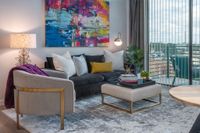 Chic and modern living room featuring vibrant artwork, plush seating, and elegant decor with abundant natural light from large windows.