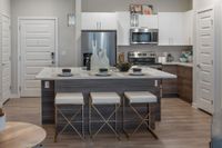 Modern kitchen with sleek stainless steel appliances, chic pendant lighting, and a stylish island with seating for three in a contemporary apartment.