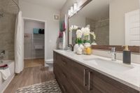 Modern bathroom with elegant vanity, dual sinks, decorative orchids, and a walk-in closet in stylish apartment.