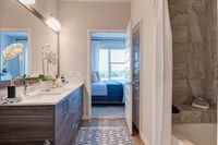 Elegant apartment bathroom with modern sink, stylish wooden cabinetry, decorative plants, and a view into a cozy bedroom with large window.