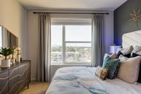 Bright and cozy bedroom with elegant decor, featuring a stylish dresser, plush pillows, and a large window offering a stunning city view.