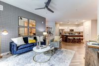 Modern living room with elegant decor, featuring a cozy blue sofa, stylish armchair, artful wall design, and open-concept kitchen with a sleek island and pendant lights.