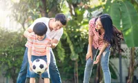woman and man helping child with soccer ball outside