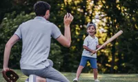 man throwing baseball at child with baseball bat outside