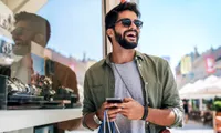 man with shopping bags and phone outside store selling watches on sunny day
