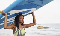 woman with surfboard over head on beach