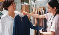 woman holding up sweater against another woman at store outdoors in daytime
