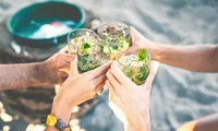 four people cheersing with drinks in hand on beach in daytime