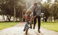 dad pushing son on bike in park