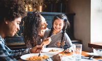 woman feeding food to child while man smiles at restaurant table