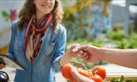 woman reaching for credit card from person holding tomatoes in outdoor market in daytime