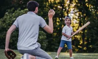man throws baseball to young boy with bat outdoors in daytime