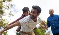 man with child on back pretending to fly outside in daytime