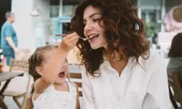young woman being fed by small child outside in daytime at restaurant