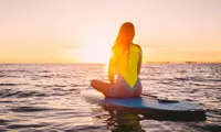 woman sitting on paddleboard in ocean at sunset