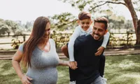 woman holding hands with young boy on man's shoulders in park in daytime