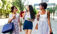 Three joyful women enjoying a day of shopping and drinks in an outdoor urban setting.